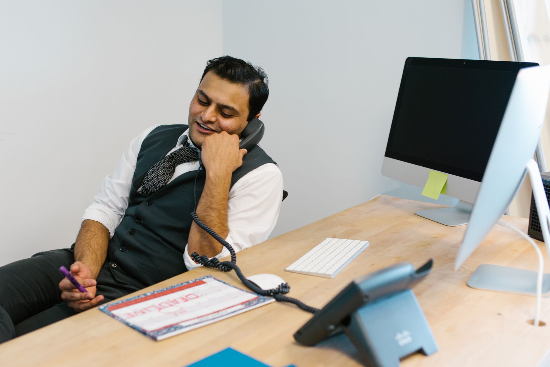 Office worker on a phone call while checking a paper calendar at a desk